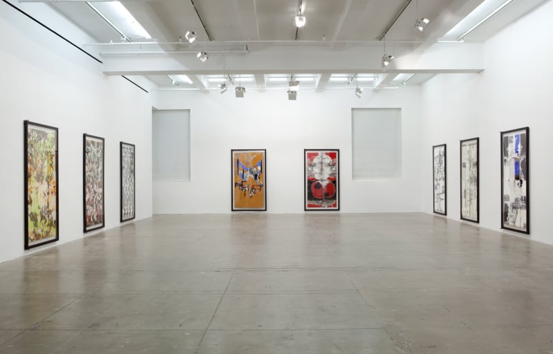 Eight large vertical abstract paintings fill the walls of a large white room. 
