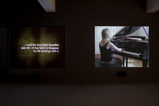 A two-video channel projection, one of an inside of a book and the other of a woman playing piano.