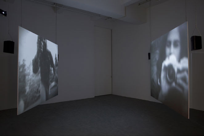 Installation view of a dark room with projections on two large suspended screens.