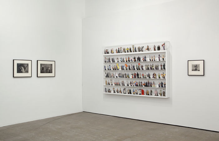 Gallery view of three framed black and white prints and a large six-tiered shelf with numerous small figurines.