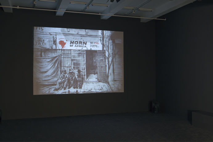 A dark room is illuminated by a projection on a wall displaying a graphic black and white illustration of three men in front of a store.  