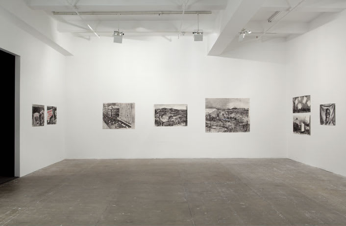 A white gallery room features various medium sized charcoal drawings on the wall. 