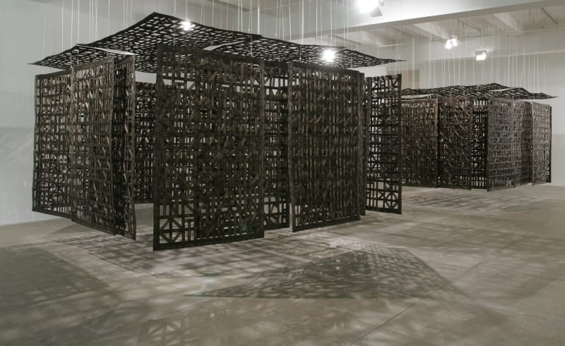 A large wooden sculpture, made up of several panels made up of wooden carved patterns which hang from the ceiling, forming a partially enclosed space.