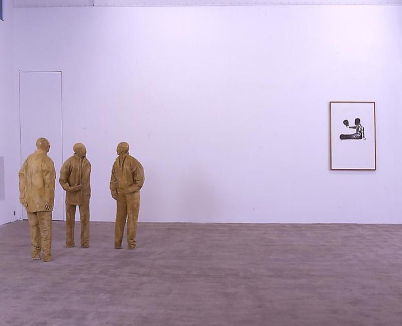 3 life size sculptures of figures stand on the left, on the right a framed drawing hangs on the wall. 