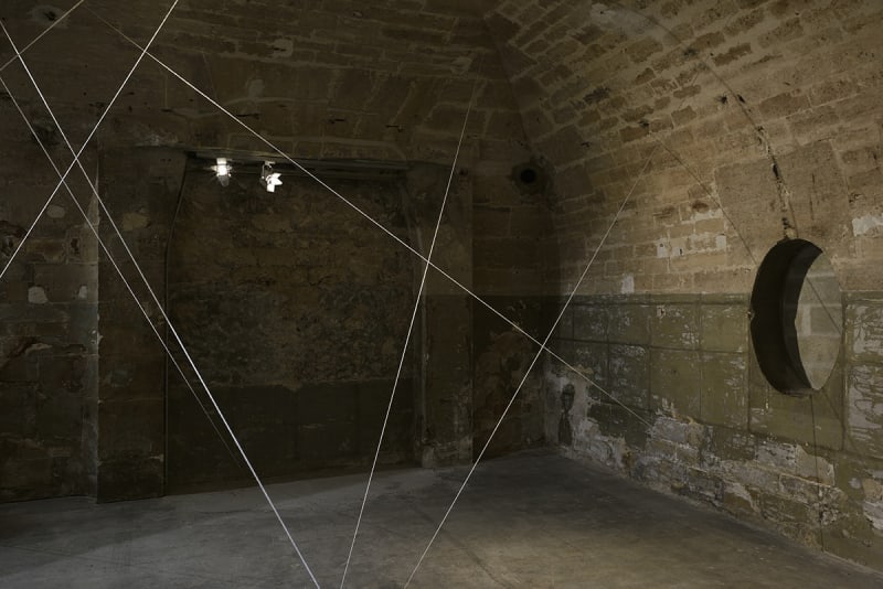 White cords are suspended in a dimly lit room with brick walls.