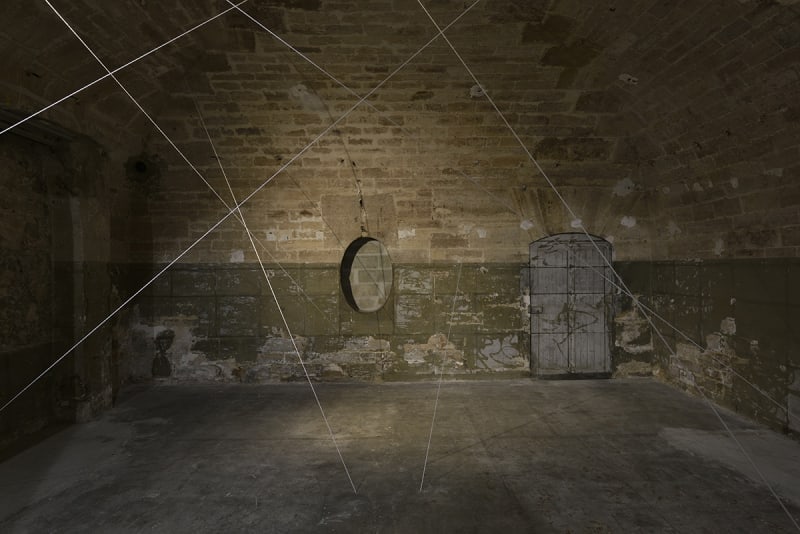 White cords are suspended in a dimly lit room with brick walls.