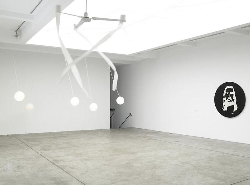 A gallery room with skylights has works hanging from the ceiling that move with the ceiling fan. 