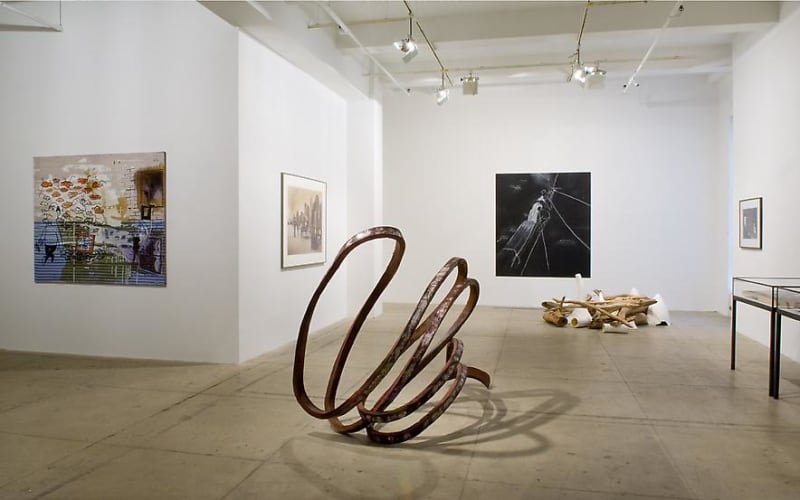 Various artworks hanging on the wall and sculptures on the floor in a clean white gallery space. 