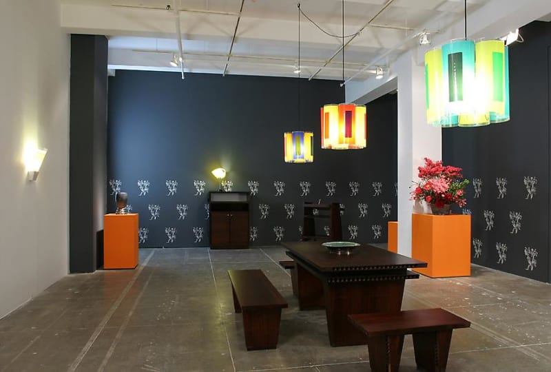 Colored lights hang above a dining room table and orange pedestals in front of a navy blue wall. 