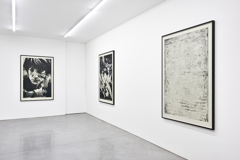 Gallery view of two vertical black and white painted portraits and one vertical abstract painting.