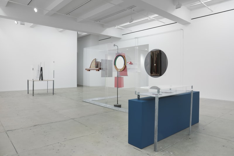 Mixed media sculptures, a bookshelf and a display case with two drawings, supported by Plexiglas walls.
