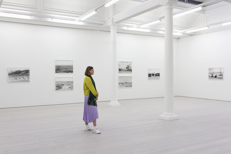A woman looks at a series of black and white photographs of war simulation by An-My Le