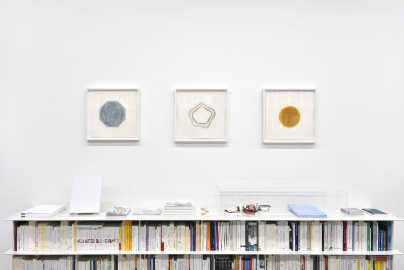 3 framed prints hanging on a white wall over bookshelves.