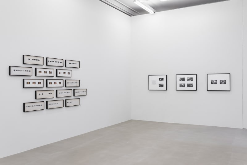 15 narrow frames holding small photographs hang three-by-three on one wall, beside one wall of large rectangular framed black and white photographs.