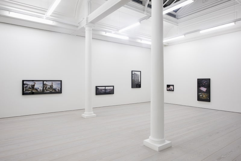A set of color photographs hang on three white walls. One on the far left is a photograph of men at work outside; the rest are images of industrial by-products.