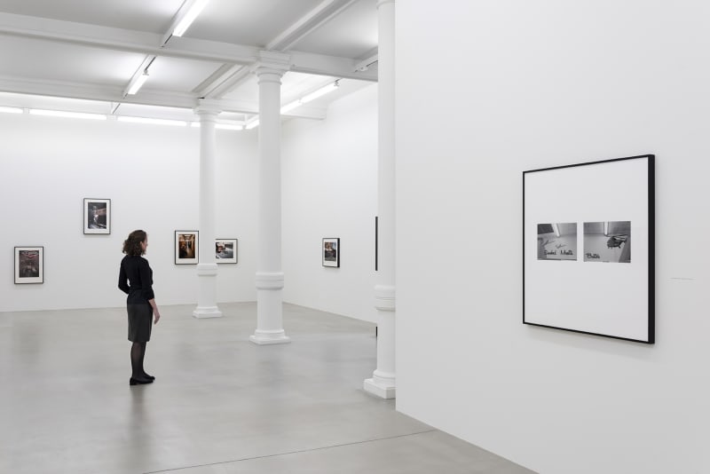 A person stands in front of a display of photographs on 2 walls.