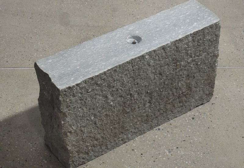 A rectangular chunk of stone with a compass imbedded on top is positioned on the ground upright. 