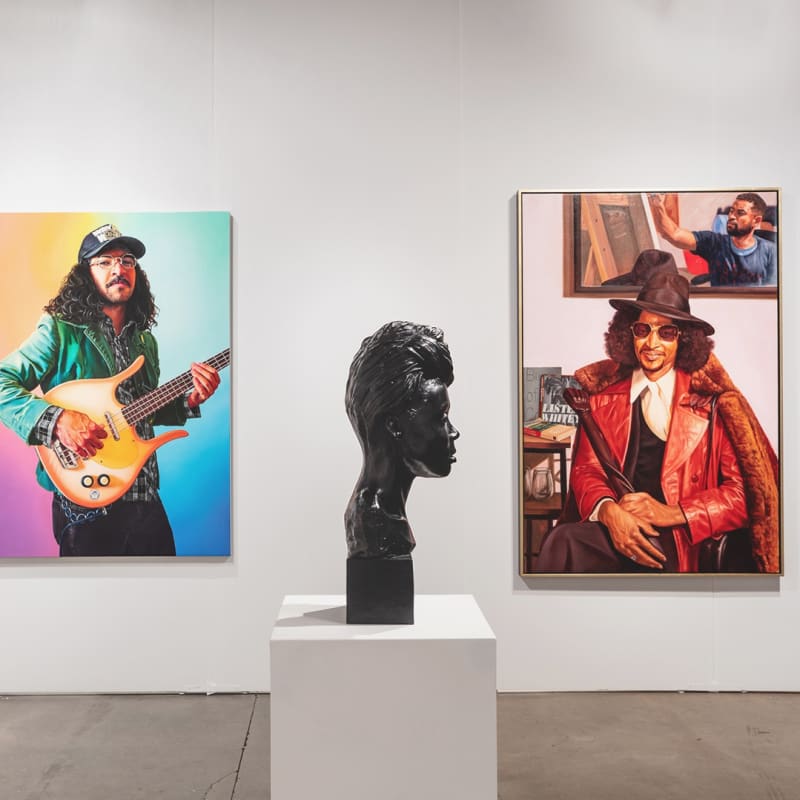 Installation view of gallery's booth at Expo Chicago art fair. The booth shows two figurative paintings hanging on the wall and a sculpture on a base in the middle