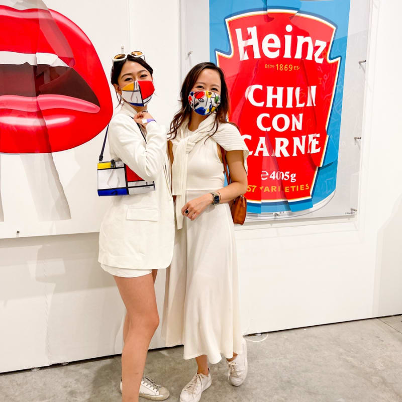 Women posing in front of paintings displayed at Carousel Fine Art's booth at the art fair, Context Art Miami 2021.