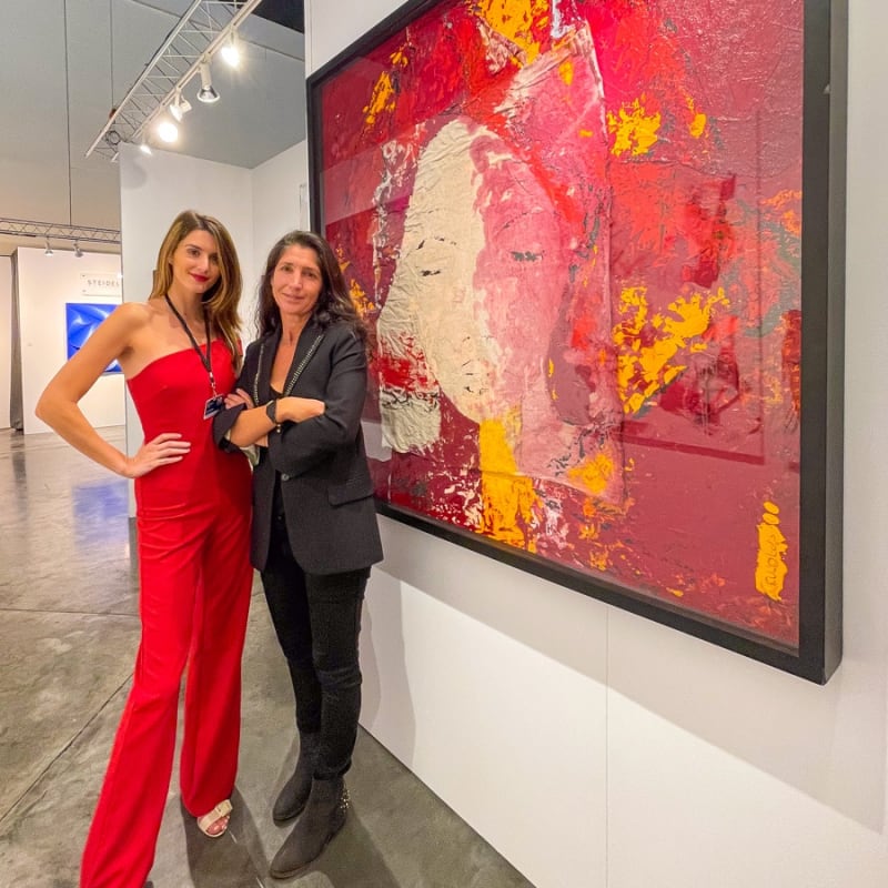 Women posing in front of paintings displayed at Carousel Fine Art's booth at the Palm Beach Show art fair, 2022.