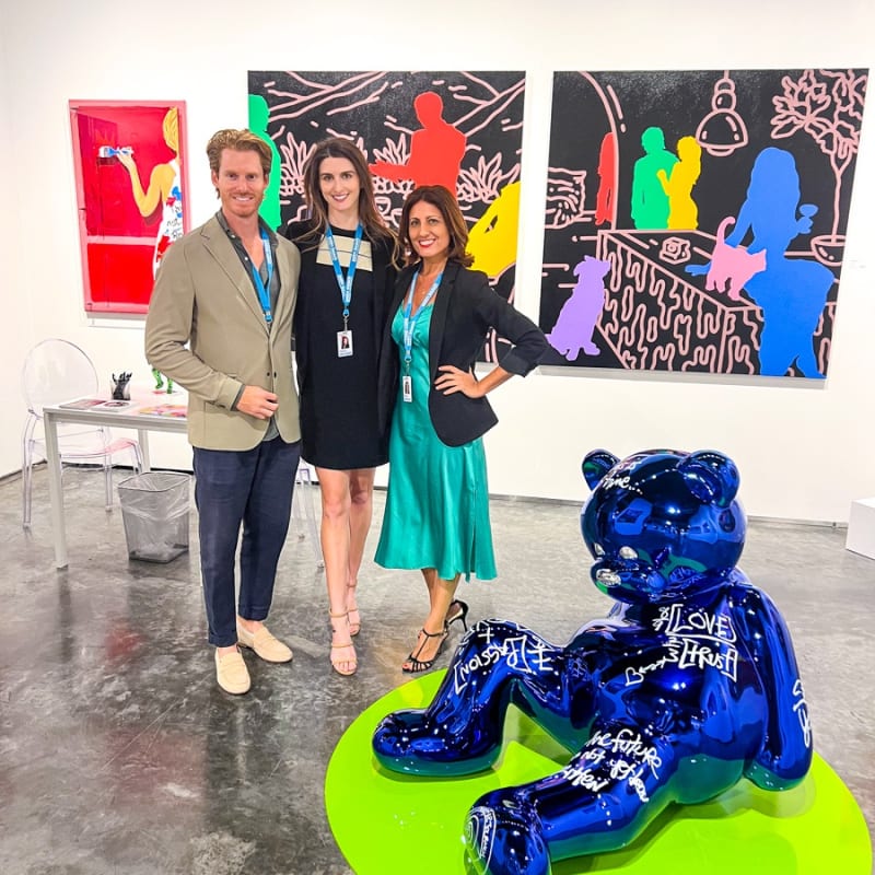 Owners of Carousel Fine Art posing at their gallery booth at the Palm Beach Modern and Contemporary art fair, 2023, surrounded by paintings and sculpture.