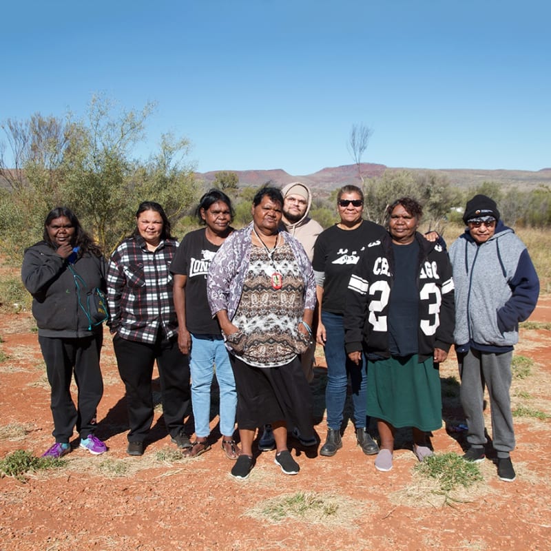 (L to R) Mandy Malbunka, Dellina Inkamala, Delray Inkamala, Vanessa Inkamala, Klinton Buzzacott (Arts Worker), Marisa Maher (Assistant Manager & Curator), Dianne Inkamala & Selma Coulthard. Photograph by Tom Nicholson in Ntaria (Hermannsburg).