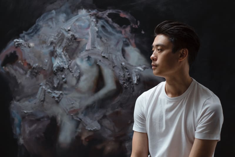 Image shows artist Henrik Uldalen sitting in front of his painting