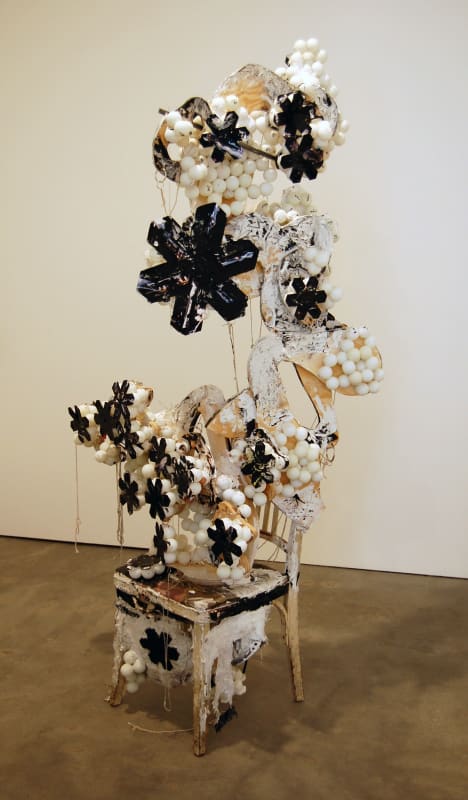 Sculpture built out of detritus coming out of a chair on the ground