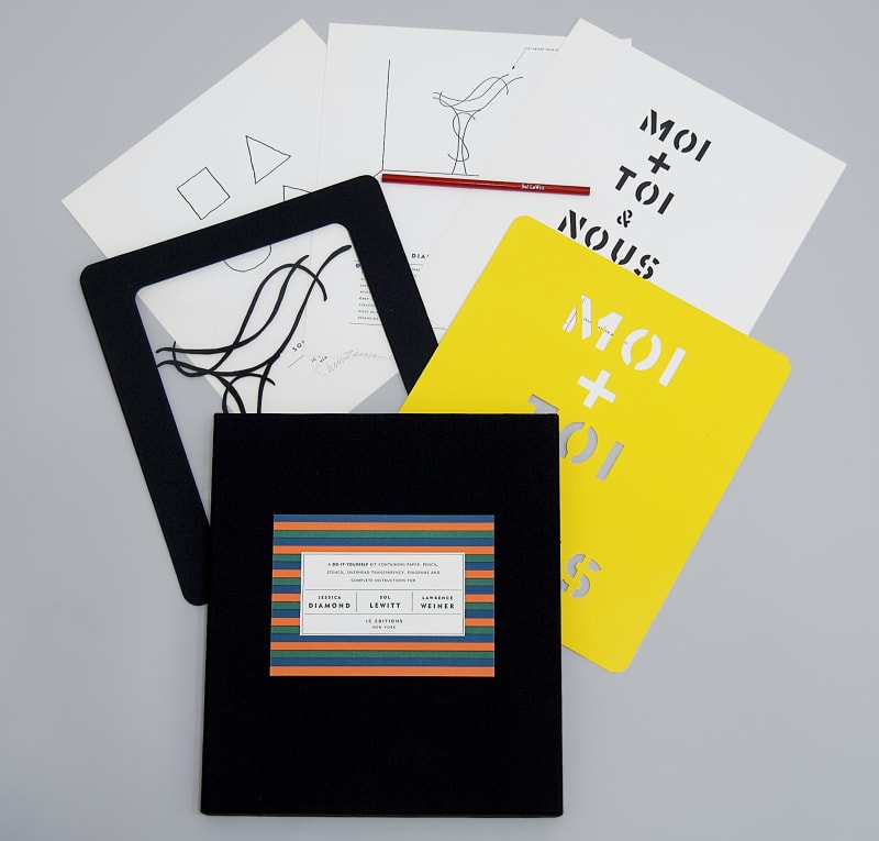 Contents of the Do It Yourself kit with projects by Jessica Diamond, Sol LeWitt, and Lawrence Weiner spread out on a grey table