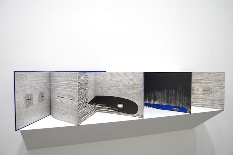 A book with accordian-bound pages presented on a white shelf 