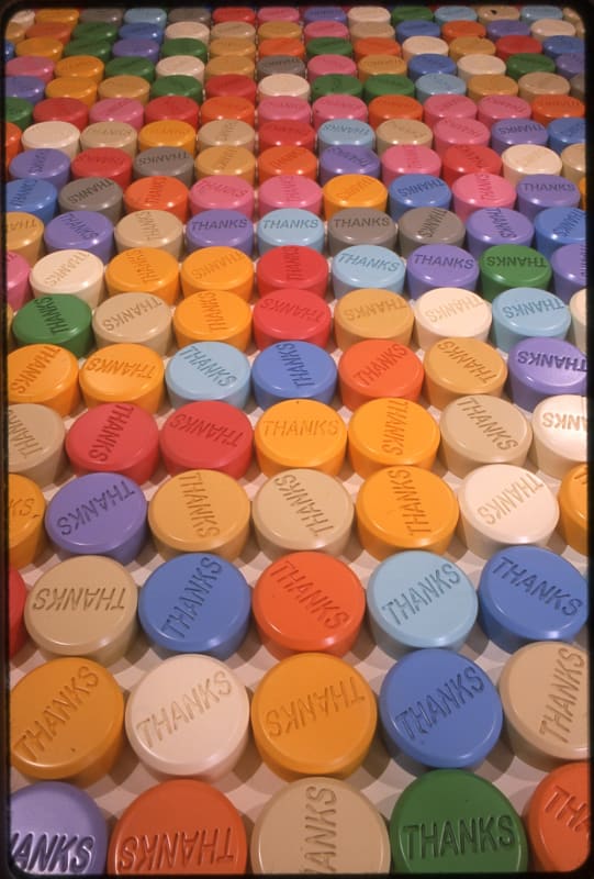 Multiple rows of multicolored puck-shaped sculptures each contain the word thanks 