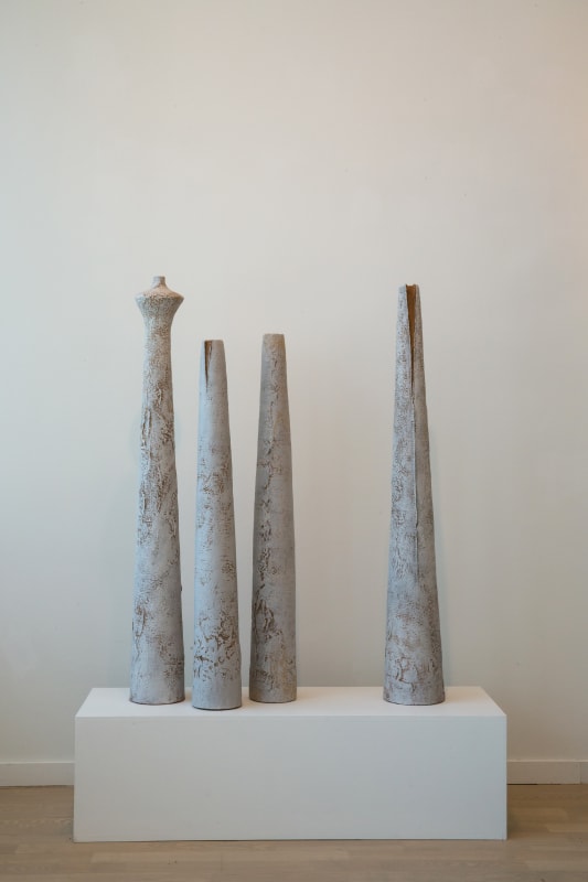 A group of Toni Ross stoneware vessels on a base set on the floor.