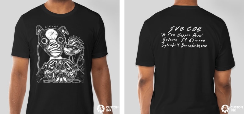 Front and back of t-shirt show; on the front, there are three dogs: one wearing a mask (text reads: clever), one half-wearing a mask (confused), and one not wearing a mask at all. The back has the name of the exhibition "It Can Happen Here, " along with t