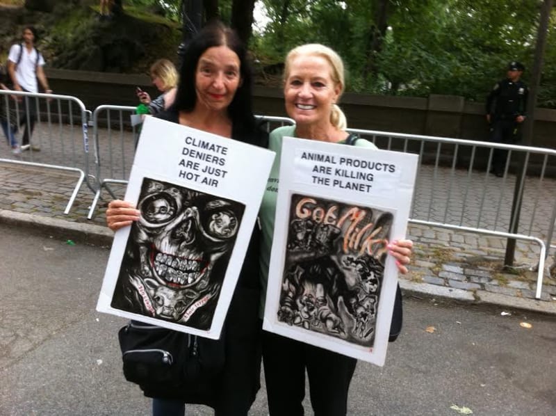 Photograph of the artist and her friend holding up signs with images from Coe's book Cruel
