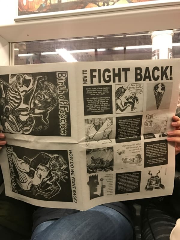 Photograph of someone on the NYC subway holding Resist!, a Mouly-designed broadsheet featuring Sue Coe's prints Birth of Fascism and Unpresidented, 2017