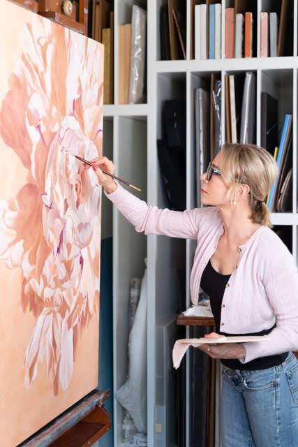 Photo of Artist Carin Gerard painting at an easel in her studio
