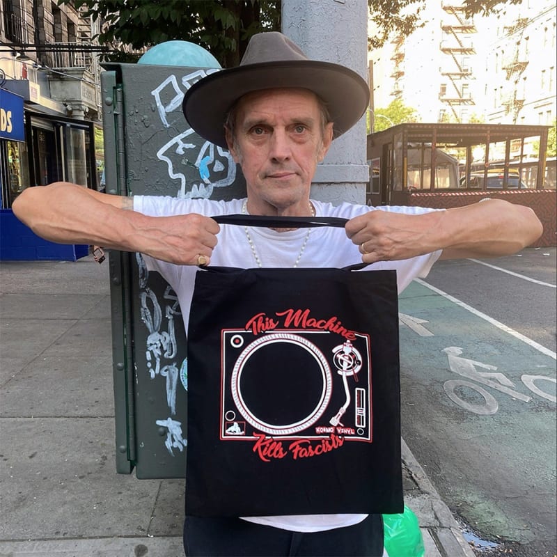 Kosmo Vinyl holding his "This Machine Kills Fascists" record tote bag