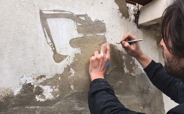 Street artist Pejac creating a mural of an excavator on a weathered wall