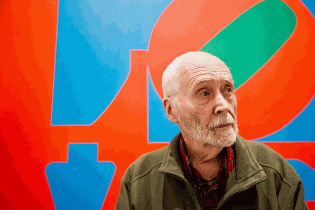 Robert Indiana with colorful abstract artwork in the background.