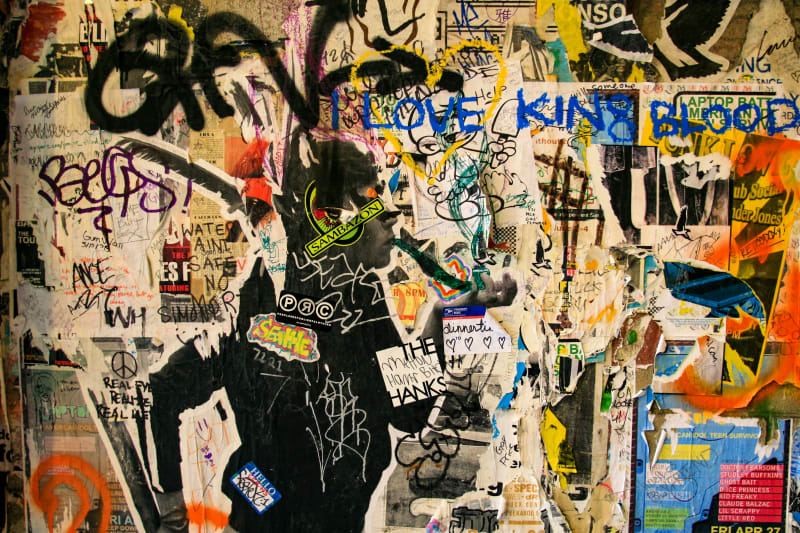 Street artists demonstrating urban art techniques with spray paint and wheatpasting creating contemporary graffiti-style artwork on wall