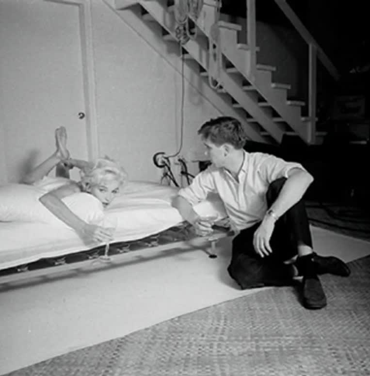 black and white photograph of Marilyn Monroe lying on her stomach in bed speaking to photographer Douglas Kirkland
