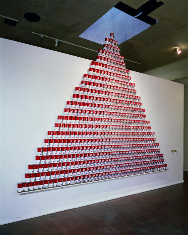 An array of red and white soup cans by artist Nobuho Nagasawa in a pyramid formation on a gallery wall
