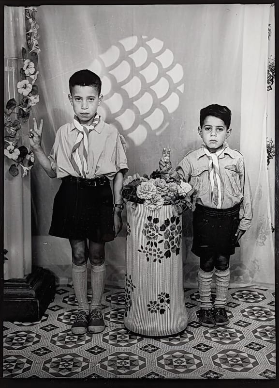 Two young boys pose for a photograph holding up a peace sign and wearing neck scarves