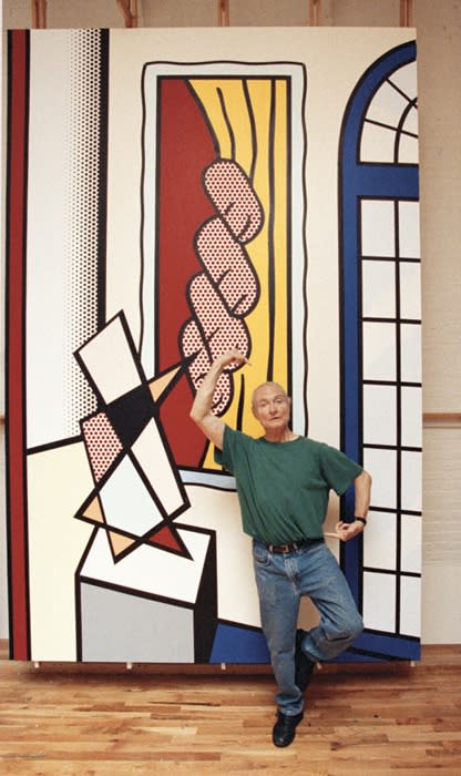 Photograph of artist Roy Lichtenstein standing in front of a painting in a studio setting