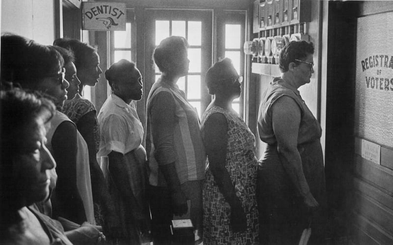 Black and white photograph of voter applicants waiting patiently in line at the Registrar of Voters office in Clinton, Louisiana