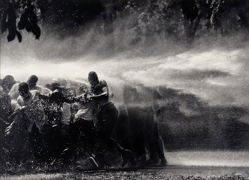Black & white photograph of African-American men and women holding each other while hosed down with water under pressure