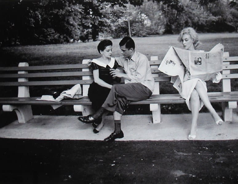 Marilyn Monroe in white dress reading a newspaper on a Central Park bench next to a couple in New York City, 1956