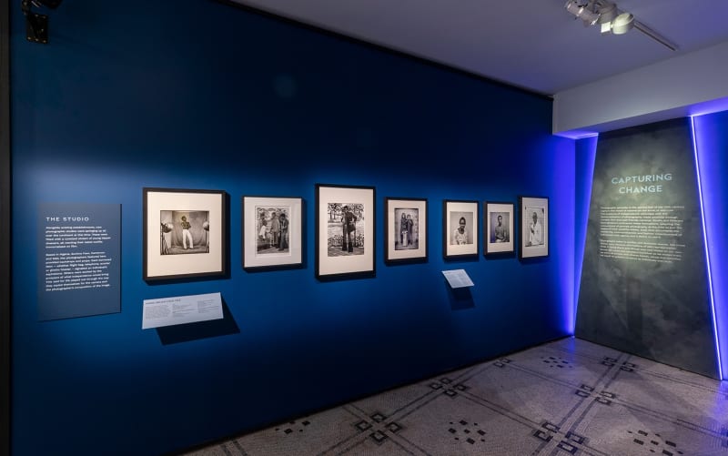 Black and white photographs in black frames hanging on a blue wall in a museum like setting