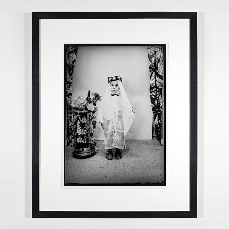 Black and white photograph of a child in local garb posing in a photo studio in Ain Beida, Algeria