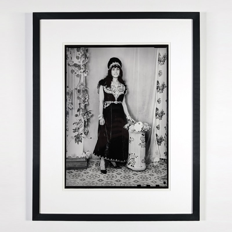 Black and white photograph of a woman in local garb posing in a photo studio in Ain Beida, Algeria